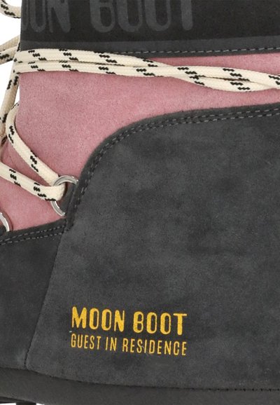 Gros plan sur une botte en daim noir et rose avec un lacet crème et le logo jaune "Moon Boot Guest in Residence" sur le côté.