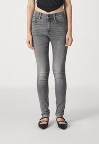 Jeans skinny de mezclilla gris con cintura alta, diseño de cinco bolsillos, un ligero desvanecimiento y detalles de costura, combinados con zapatos planos negros de punta.