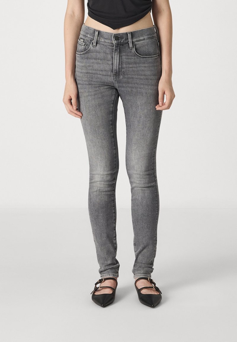 Jeans skinny de mezclilla gris con cintura alta, diseño de cinco bolsillos, un ligero desvanecimiento y detalles de costura, combinados con zapatos planos negros de punta.