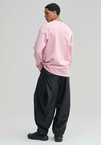 Világos rózsaszín, hosszú ujjú, laza fazonú ing, fekete, bő szabású nadrággal párosítva. Az öltözéket fekete sportcipőkkel egészítik ki.