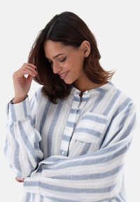 Camicia leggera a maniche lunghe in lino a righe blu e bianche. Presenta un colletto rotondo, chiusura con bottoni e una tasca sul petto.