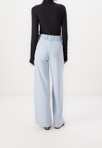 Světle modré široké kalhoty s elastickým pasem, spárované s přiléhavým černým topem s dlouhým rukávem. Hladký materiál, jednoduchý design.