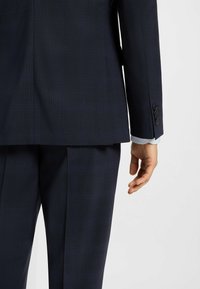 Marinblå rutigt kostym med en texturerad yta. Jackan har rak skärning, lång ärm och knapprad på manschetterna.