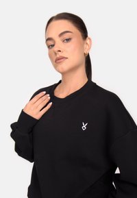 Fekete, túlméretezett, pamut keverékből készült pulóver, kerek nyakkivágással, bal mellkasán egy kis fehér logóval és bordázott mandzsettákkal.