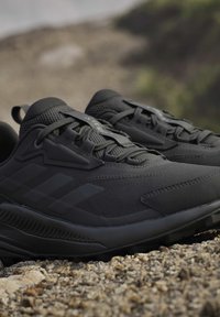 Paar zwarte sportschoenen met gestructureerde mesh stof en dikke zolen die op grind buiten rusten.