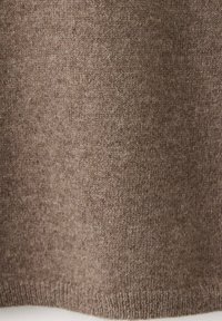 Gros plan sur un tissu tricoté marron doux avec un ourlet côtelé, montrant une texture détaillée et des coutures fines.