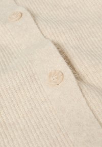 Cremefarvet cardigan med struktureret strikket stof og en række af tre lyse knapper langs frontåbningen.