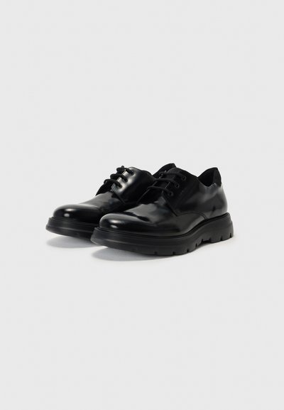 Black leather shoes with a glossy finish, round toe, lace-up design, and thick rubber sole featuring a textured tread pattern.