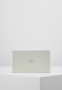 Boîte cadeau Fossil en matériau texturé blanc, arborant un petit logo doré en forme de diamant et un design rectangulaire épuré.
