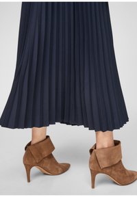 Jupe midi plissée bleu marine associée à des bottines marron en daim à talons hauts avec de larges revers pliés.