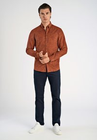 Bruine geblokte overhemd met rechte snit, gecombineerd met marineblauwe broek en witte sneakers. Vloeiende textuur, eenvoudige knopen.