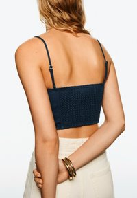 Mornarskopravi cropped top s teksturom i nabranim dizajnom, podesivim naramenicama i ravnim rubom, u kombinaciji sa bež hlačama visokog struka.