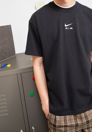 Camiseta de algodón negra con cuello redondo y mangas cortas, que presenta un logo blanco de Nike "AIR" centrado en el pecho.