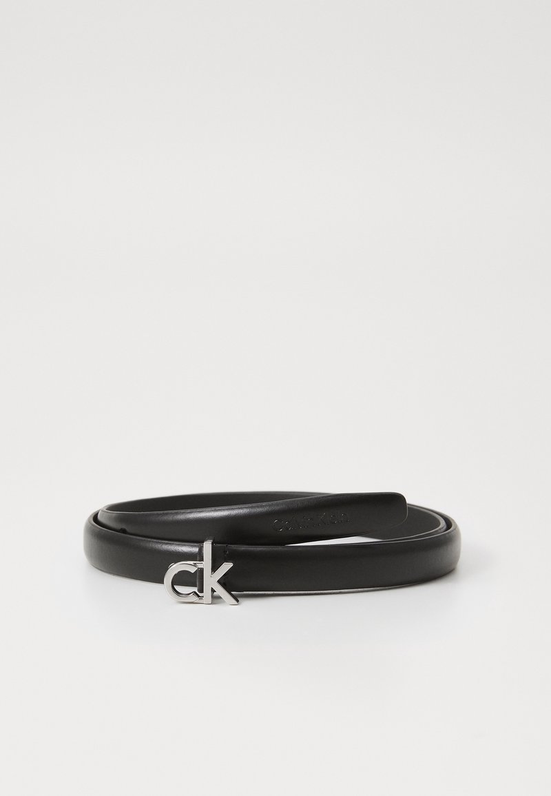 Ceinture fine en cuir noir enroulée avec boucle argentée stylisée "ck" sur un fond blanc uni.