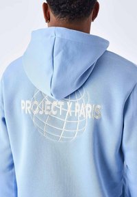 Sudadera azul claro hecha de tela suave. Presenta un gran texto bordado en blanco "PROJECT X PARIS" y un diseño de globo en la parte posterior.
