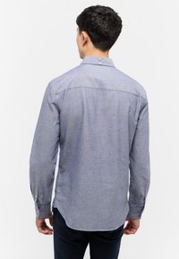 Niebieska koszula z guzikami wykonana z textured materiału, z regularnym kołnierzykiem, długimi rękawami i zaokrąglonym dołem. Tył z subtelnym detalem wyszycia.