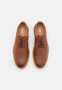 Scarpe in pelle marrone con una superficie liscia, dotate di lacci marroni, punta arrotondata e cucitura crema sulla suola. Logo impresso all'interno.