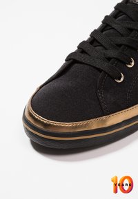 Schwarze Leinensneaker mit einem metallisch goldenen Akzent an der Zehenkappe, strukturiertem Gummisohle und schwarzen Schnürsenkeln. Verfügt über ein glattes, elegantes Design.