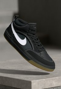 Høye sneakers laget av svart semsket skinn og mesh med en hvit Nike-logo, gummisåle og kontrasterende sømdetaljer.