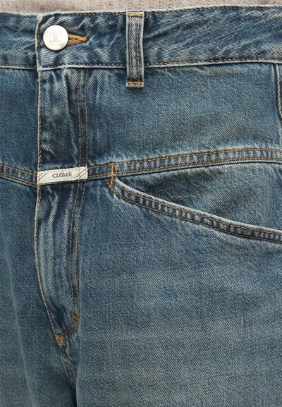 Jean en denim bleu clair avec une coupe standard, poche avant, coutures orange et une petite étiquette "CLOSED" près de la ceinture.