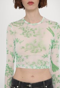Tynn, langermet crop top i lett stoff med grønt blomstermønster. Har rund hals og trykte detaljer på skulderen.