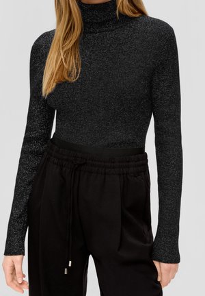 Femme portant un pull à col roulé noir ajusté et pailleté ainsi qu'un pantalon noir ample avec cordon, montrée du cou aux hanches.