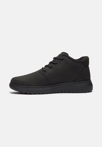 Chaussure décontractée noire montant à la cheville avec fermeture à lacets, bout arrondi, col rembourré et semelle épaisse en caoutchouc sur fond clair uni.