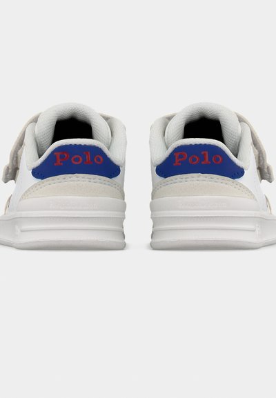 Άσπρα αθλητικά παπούτσια με μπλε ταμπελάκια στη φτέρνα και κόκκινη σήμανση "Polo", παρουσιάζονται από πίσω σε απλό λευκό φόντο.