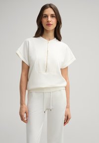 Witte zip-up top met korte opgerolde mouwen en een vierkante voorzak; gecombineerd met bijpassende witte joggers met verstelbare trekkoord.