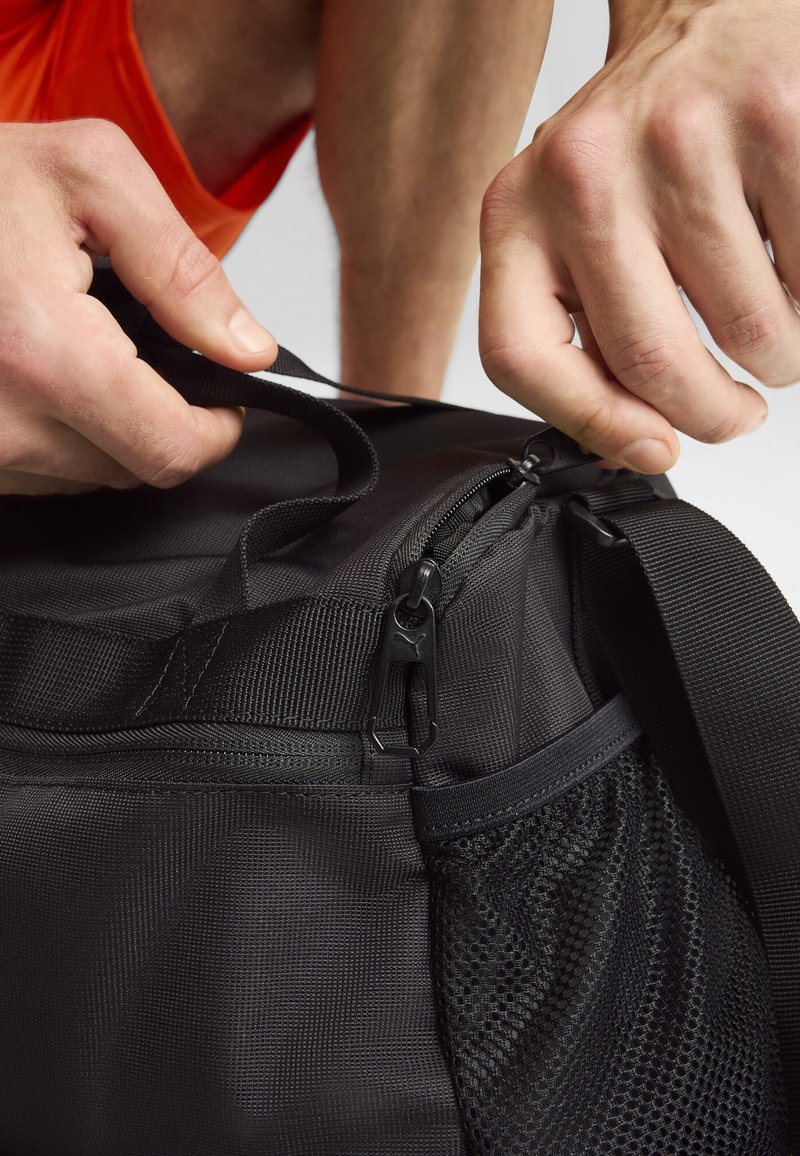 Zwarte sport duffel bag van textuurstof, met een mesh zijvak, stevige schouderriem en ritssluiting, met een slank ontwerp en duurzame hardware.