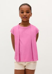 Light pink cotton t-shirt with short sleeves and a draped design at the front. Paired with cream-colored shorts with distressed hem.