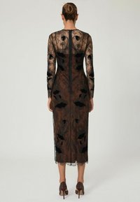 Juoda nėrinių suknelė su ilgomis rankovėmis, sudėtingais gėlių raštais ir prigludusia siluetu, pasižyminti skaidriu audiniu ir iki kelių ilgiu.