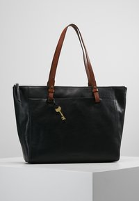Sac fourre-tout en cuir noir avec des poignées en cuir marron. Comprend une poche latérale zippée et un porte-clés décoratif en or attaché. Texture lisse, forme structurée.