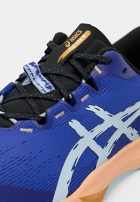 Asics Fuji Lite 6 sko har en blå mesh-overdel med sorte detaljer, struktureret overflade, lyseblå logo og orange mærke. Sålen er lys tan.