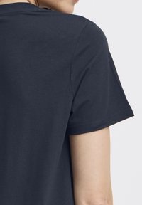 Tmavě modré bavlněné tričko s krátkými rukávy a kulatým výstřihem. Hladká textura s jednoduchým, čistým designem a minimálními detaily švů.