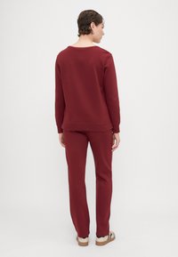Bordowy dres składający się z bluzy z okrągłym dekoltem i dopasowanych spodni, cechujący się luźnym krojem i miękką fakturą. Minimalistyczny design bez widocznych logo.