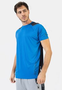 Camiseta atlética azul con detalles en negro, hecha de un material ligero y transpirable. Presenta un logo en el lado izquierdo y un escote redondo.