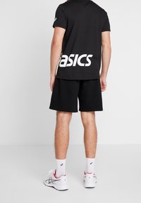 Black cotton t-shirt with "basics" in large white letters on the back, paired with black shorts and white athletic shoes with red accents.
