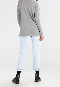 Szary długi rękaw top z obniżonymi ramionami, połączony z jasnoniebieskimi spodniami typu cuffed i czarnymi botkami za kostkę z bocznymi zamkami.