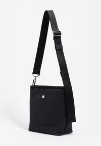 Czarna torba typu crossbody z płaskim designem, regulowanym paskiem, przednią kieszenią oraz metalowym zapięciem na zatrzask. Gładka tekstura.