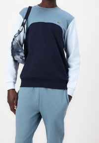 Felpa in tonalità blu con un design a blocchi di colore, con una parte anteriore blu scuro e maniche azzurre. Abbinata a pantaloni jogging blu coordinati.