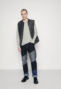 Juoda dygsniuota liemenė dėvima ant šviesiai pilkos, ilgomis rankovėmis marškinėlių, derinama su tamsiomis džinsais su lopais ir juodais raišteliais užsegamais aulinukais. Paprastas dizainas ir praktiška išvaizda.