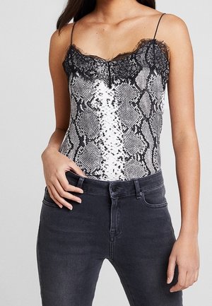 Bodysuit en imprimé serpent noir et blanc avec bordure en dentelle, fines bretelles et design ajusté, associé à un jean gris foncé.