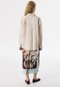 Jasno beżowa koszula zapinana na guziki z plisą z tyłu. Połączona z nadrukowaną spódnicą w ciemne i jasne kolory, z rozcięciem na tylnym brzegu.