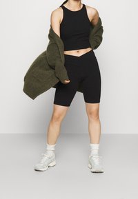 Svart ribbad croppad topp, högmidjade svarta cykelbyxor, oversized olivgrön cardigan och ljusa sneakers med texturerade detaljer.