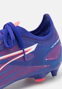 Purple soccer cleat featuring a textured upper, pink and blue accents, and a streamlined design with a white logo on the side.