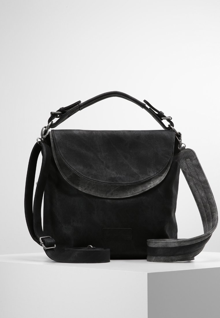 Sac à bandoulière en cuir noir avec fermeture à rabat, poignée supérieure et bandoulière longue réglable posé sur un socle blanc contre un fond uni.