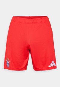 Röda sportshorts i slätt tyg, med en broderad logotyp och fem stjärnor ovanför, samt vita Adidas-ränder på sidan.