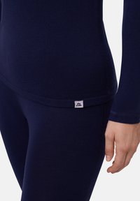 Navyblaues Langarmoberteil mit taillierter Passform, aus glattem Stoff gefertigt und mit einem kleinen Markenetikett am Saum.