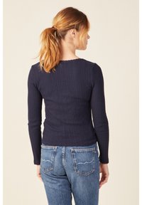 Maglietta a maniche lunghe a coste blu navy con scollatura ondulata, abbinata a jeans in denim blu a vita alta con doppie tasche posteriori e cuciture sottili.